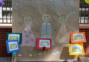 Plakat z napisem Dzień Przedszkolaka oraz pięć tabliczek z nazwami grup