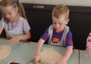 Dziewczynki i chłopiec wyrabiają ciasto na pizzę