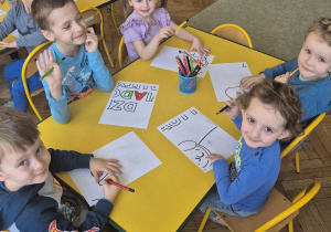 Dzieci siedzą przy tole i kolorują